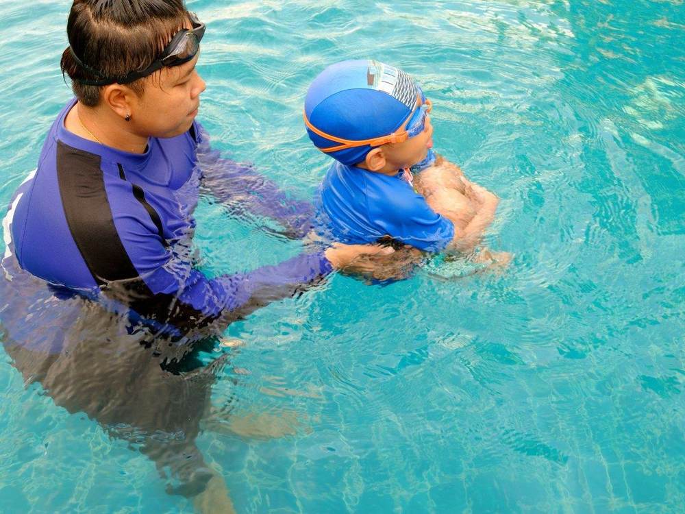 An instructor holding a toddler in a swim cap in the water